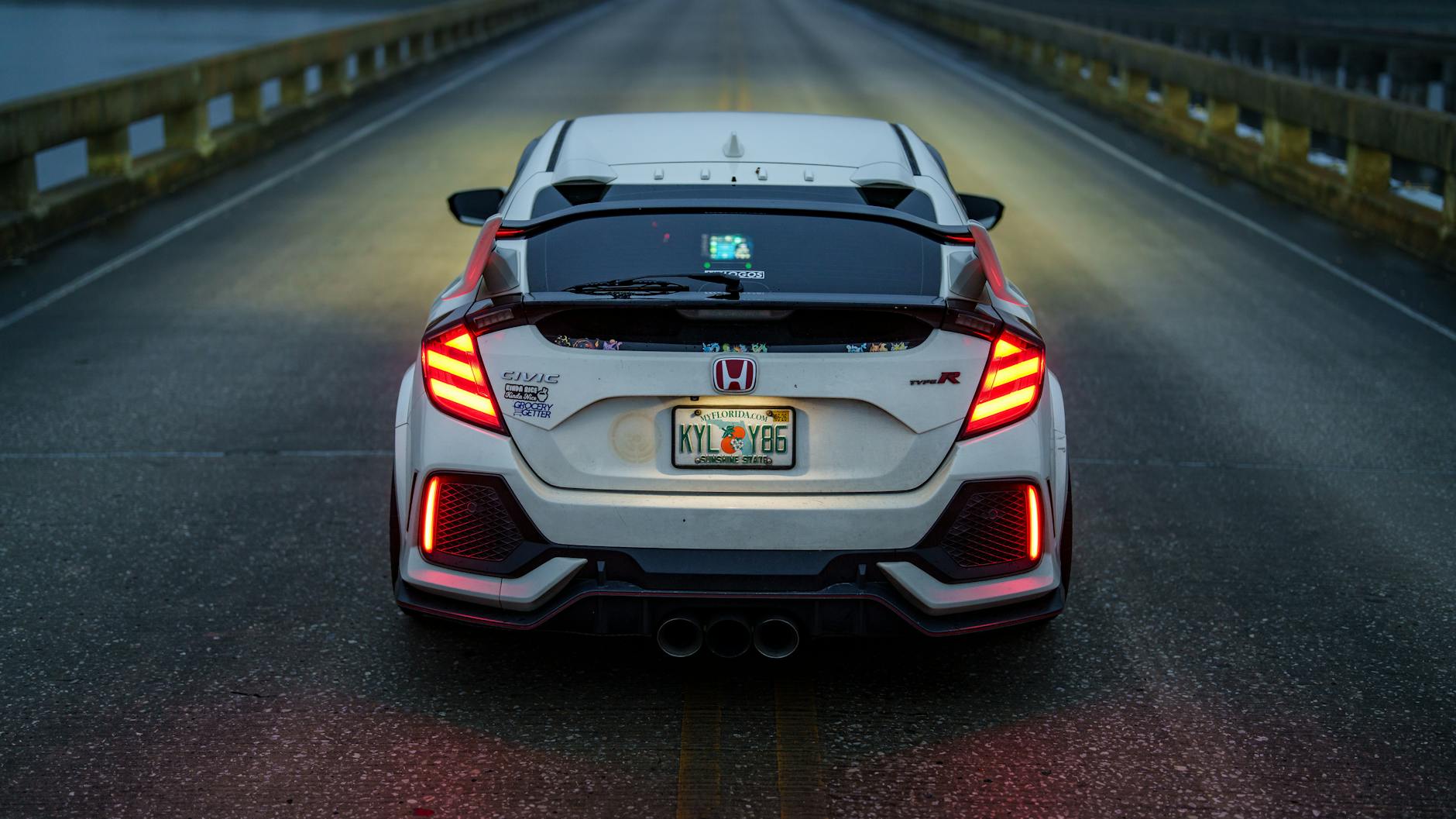 Białe sportowe auto na moście nocą, widok od tyłu z włączonymi światłami