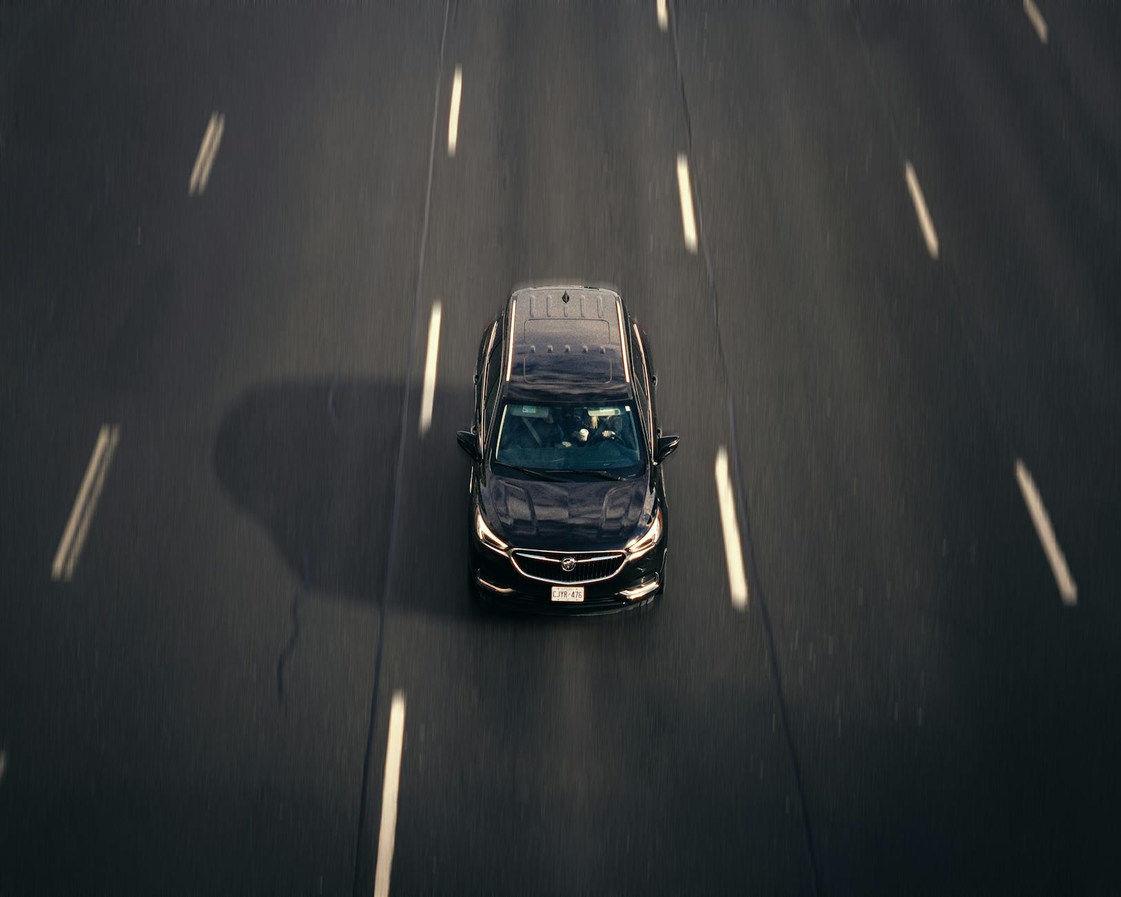 Auto „tańczy” na autostradzie: jak po objawach ustalić, czy winne są opony, felgi czy geometria Czarny samochód jadący autostradą w mieście z lotu ptaka