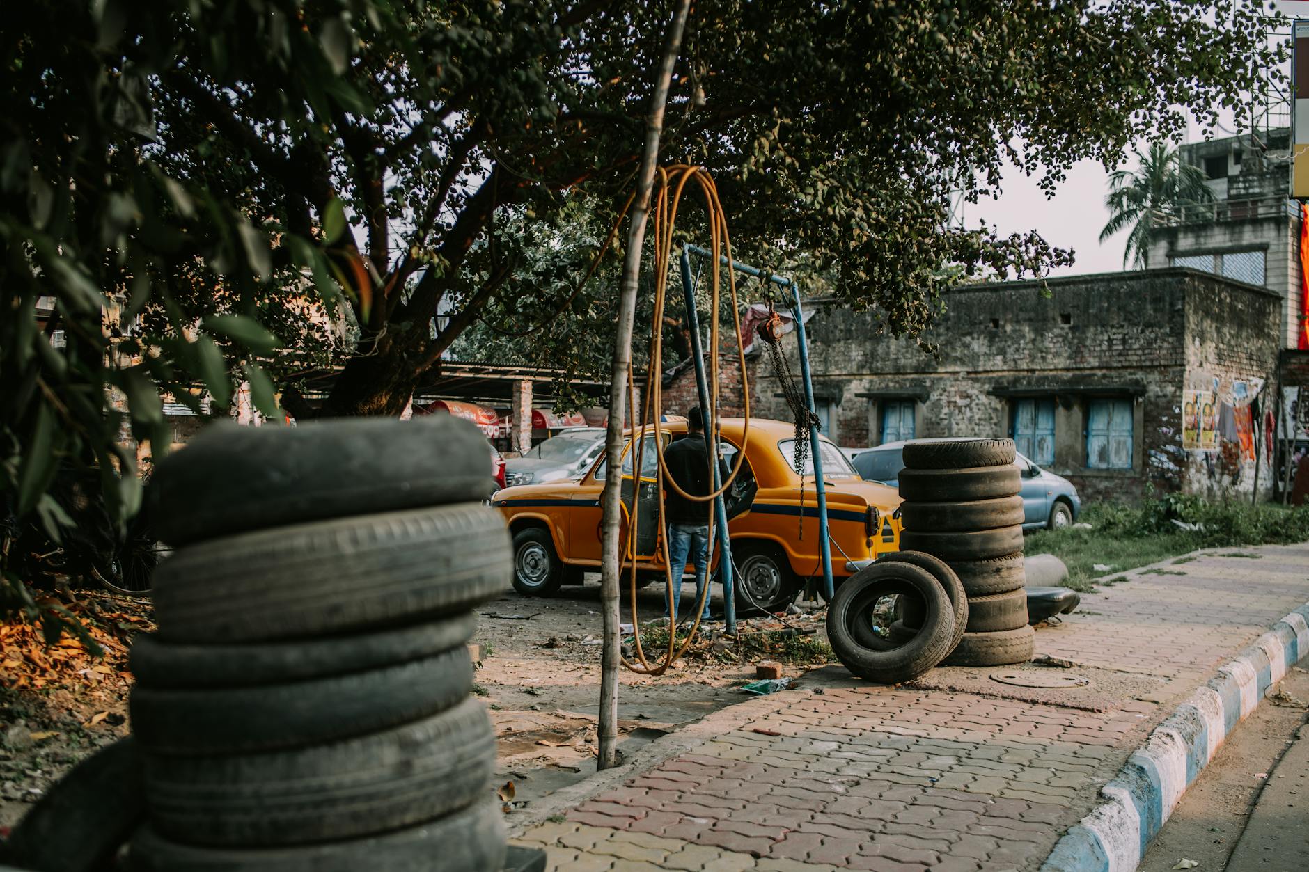 Mechanik przy stosie opon pracuje przy aucie zaparkowanym pod drzewem