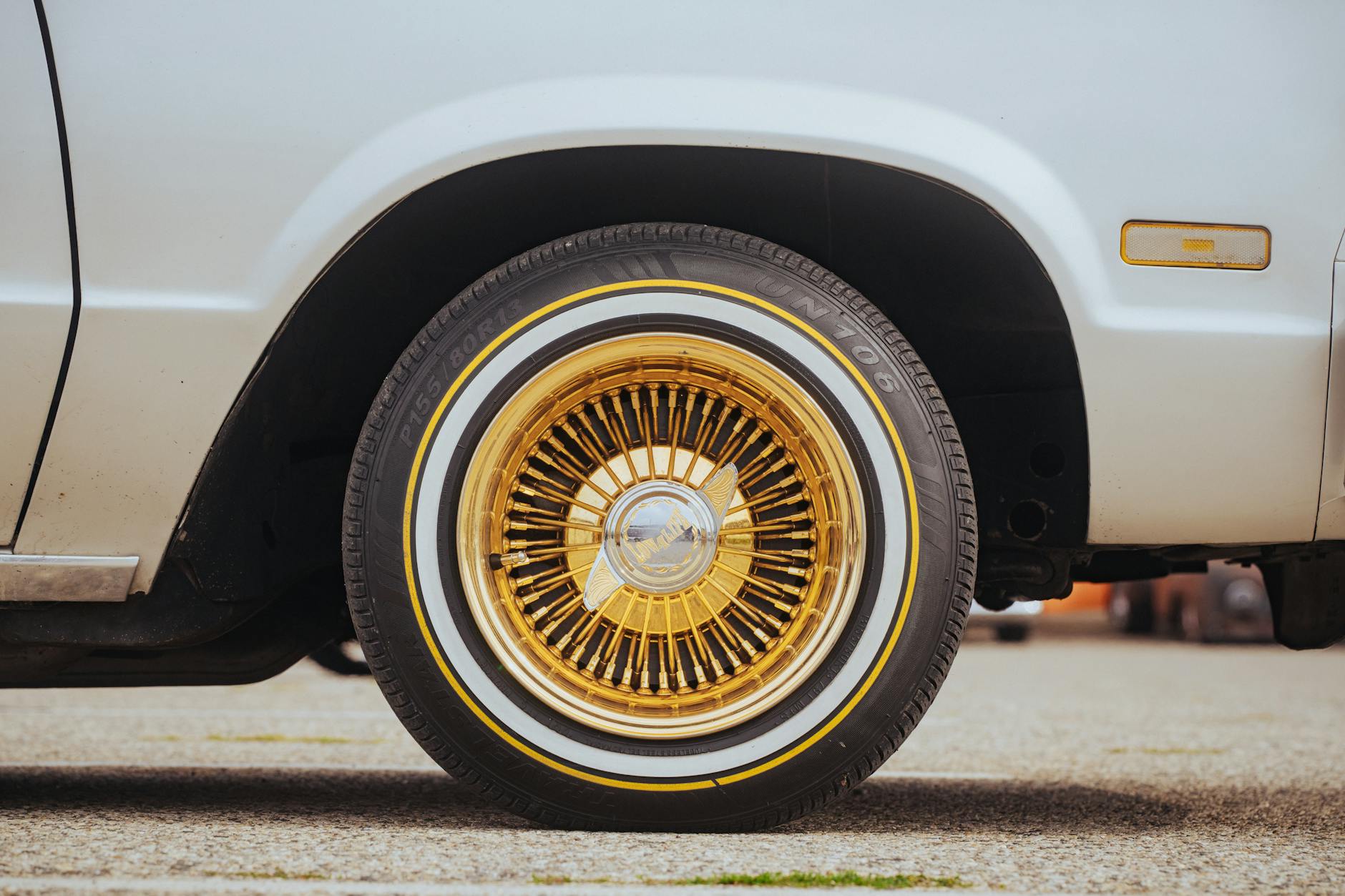 Zbliżenie na złotą szprychową felgę klasycznego auta z oponą białą
