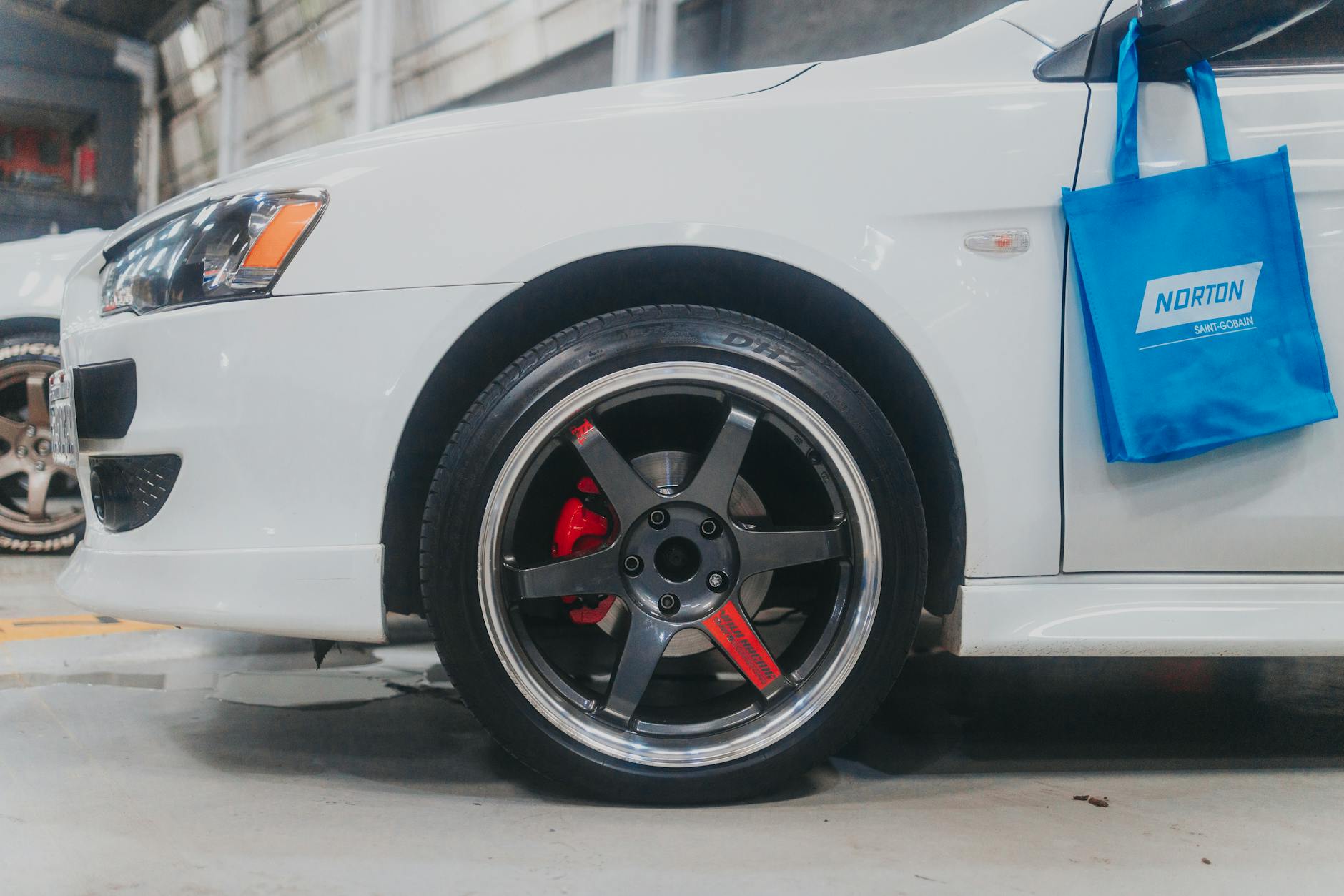 Zbliżenie na aluminiową felgę białego auta z widocznym zaciskiem hamulcowym