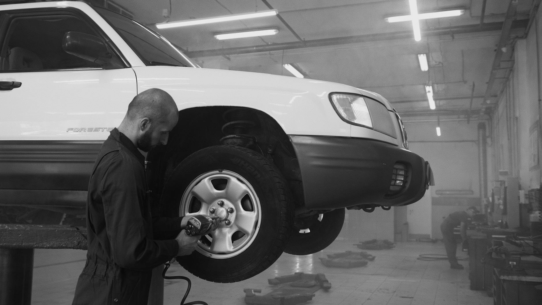 Mechanik dokręca koło kluczem udarowym w warsztacie samochodowym
