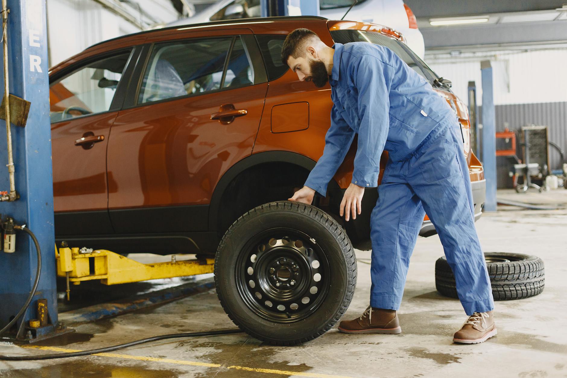 Mechanik wymienia oponę w czerwonym SUV-ie w warsztacie samochodowym