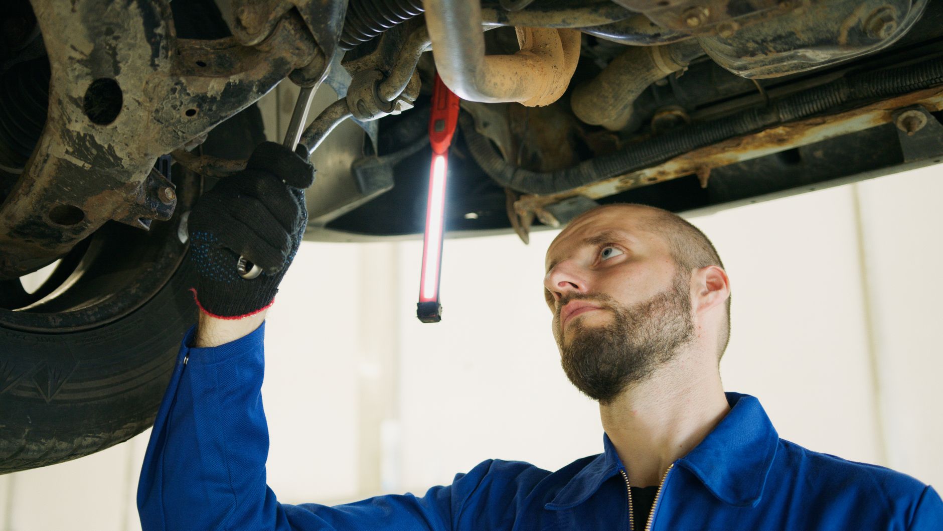 Mechanik serwisujący auto pod podnośnikiem w warsztacie samochodowym Mechanik serwisujący auto pod podnośnikiem w warsztacie samochodowym