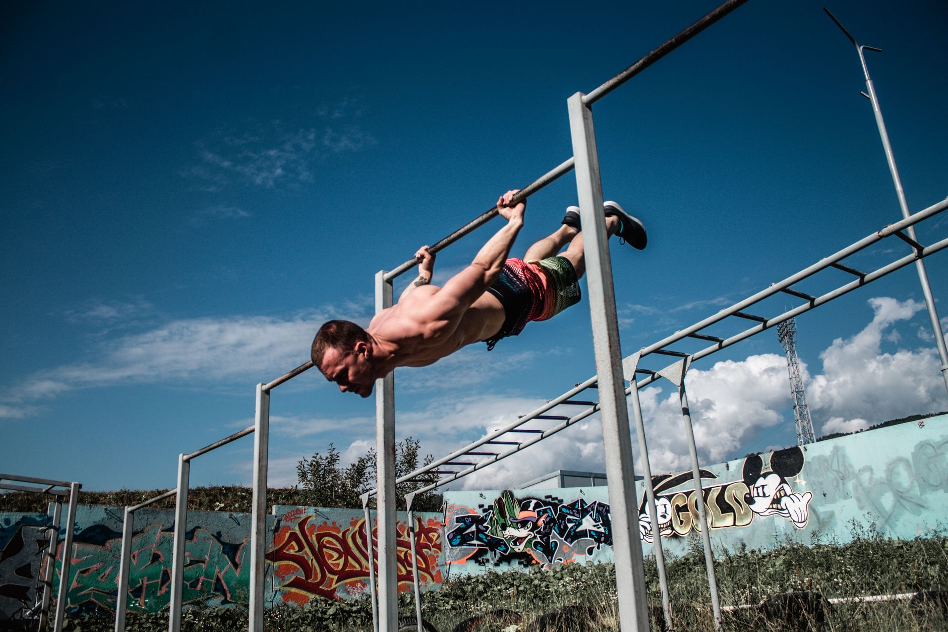 Mężczyzna wykonuje human flag na drążku na tle ściany z graffiti Mężczyzna wykonuje human flag na drążku na tle ściany z graffiti
